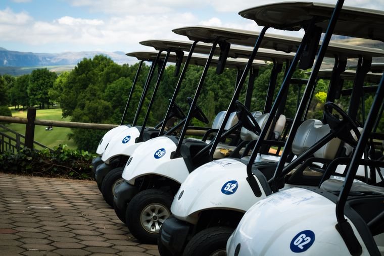 A row of white electric golf cart battery vehicles lined up at a facility between shifts